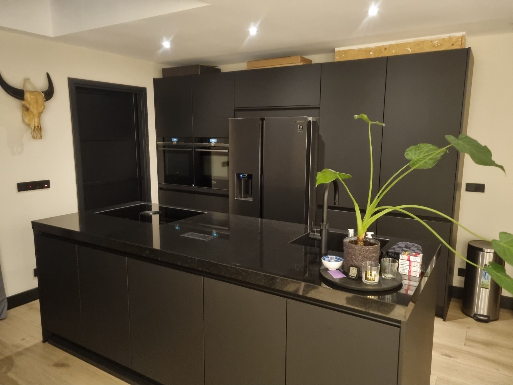 Afgewerkte zwarte keuken met kookeiland, verlichting en elektrotechnische aansluitpunten
